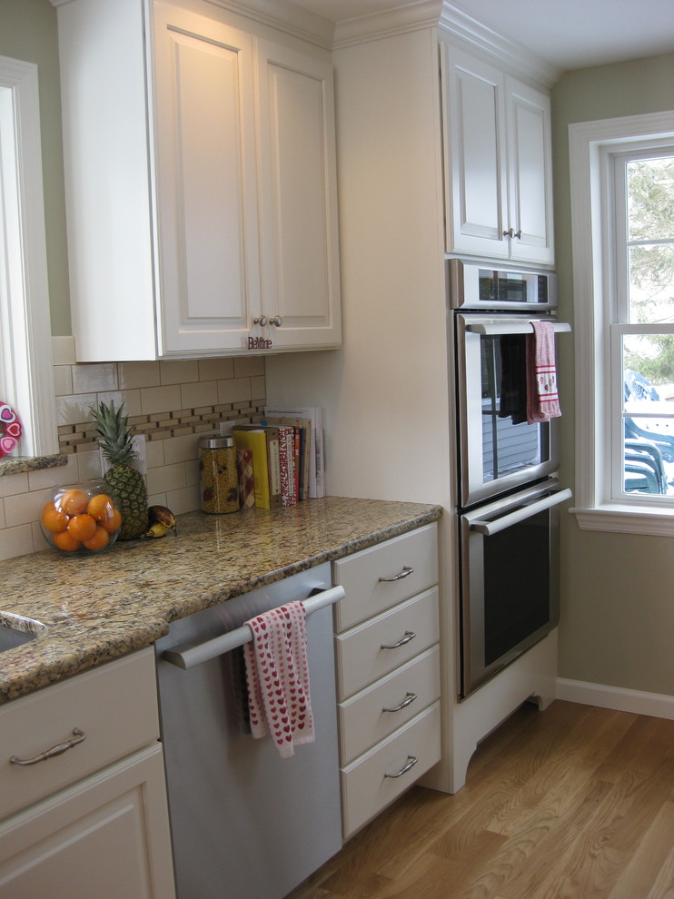 Inspiration for a transitional u-shaped medium tone wood floor eat-in kitchen remodel in Boston with an undermount sink, raised-panel cabinets, white cabinets, granite countertops, white backsplash, ceramic backsplash, stainless steel appliances, an island and beige countertops