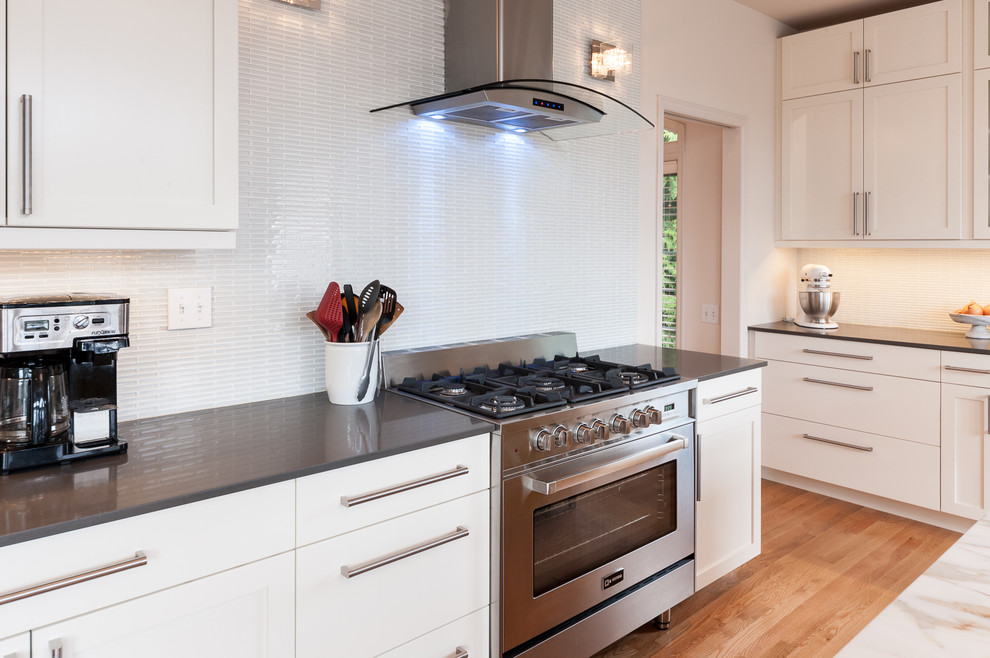 This is an example of a mid-sized modern l-shaped open plan kitchen in Seattle with a double-bowl sink, shaker cabinets, yellow cabinets, marble benchtops, white splashback, glass tile splashback, stainless steel appliances, light hardwood floors and with island.