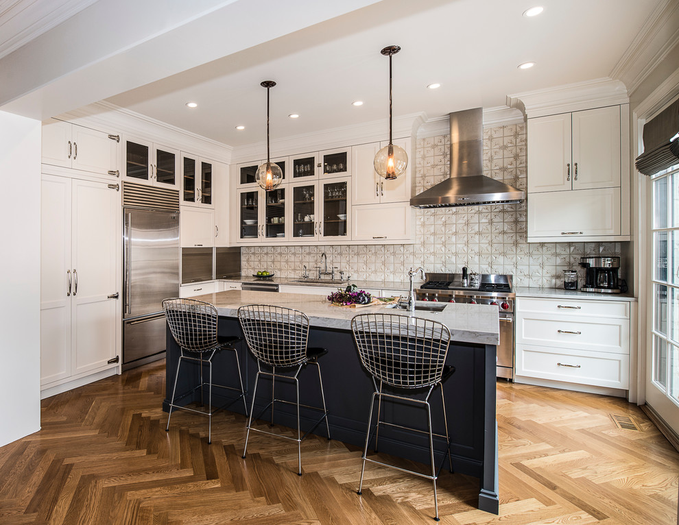 Mid-sized transitional l-shaped medium tone wood floor and brown floor kitchen photo in Chicago with an undermount sink, white cabinets, granite countertops, beige backsplash, stainless steel appliances, an island, shaker cabinets and gray countertops