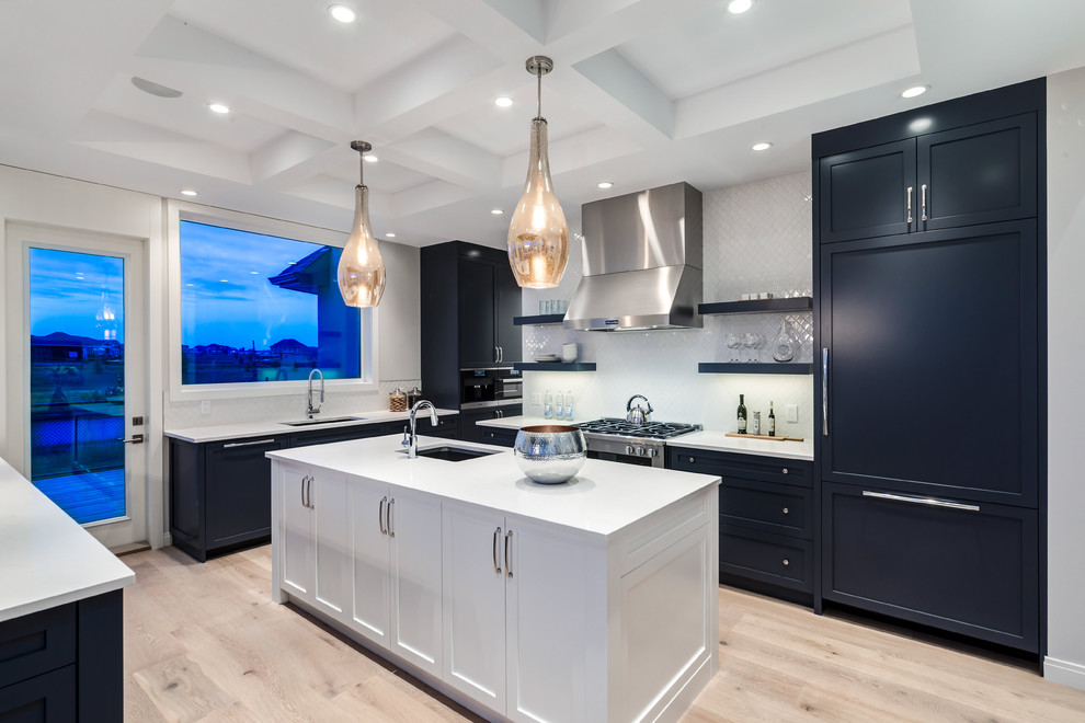 Example of a transitional u-shaped light wood floor kitchen design in Calgary with an undermount sink, shaker cabinets, blue cabinets, quartzite countertops, white backsplash, porcelain backsplash, stainless steel appliances and an island