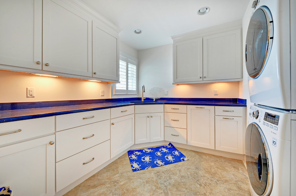 Photo of a beach style l-shaped laundry room in Philadelphia with a stacked washer and dryer and blue benchtop.