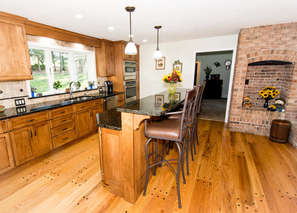 Mid-sized traditional galley eat-in kitchen in Philadelphia with an undermount sink, flat-panel cabinets, brown cabinets, granite benchtops, black splashback, stone tile splashback, stainless steel appliances, light hardwood floors, with island and beige floor.