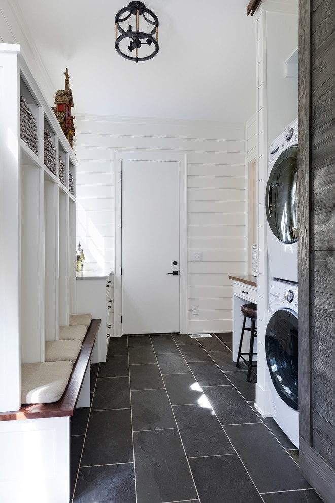 Photo of a large beach style galley utility room in Minneapolis with white cabinets, wood benchtops, white walls, slate floors, a stacked washer and dryer and grey floor.