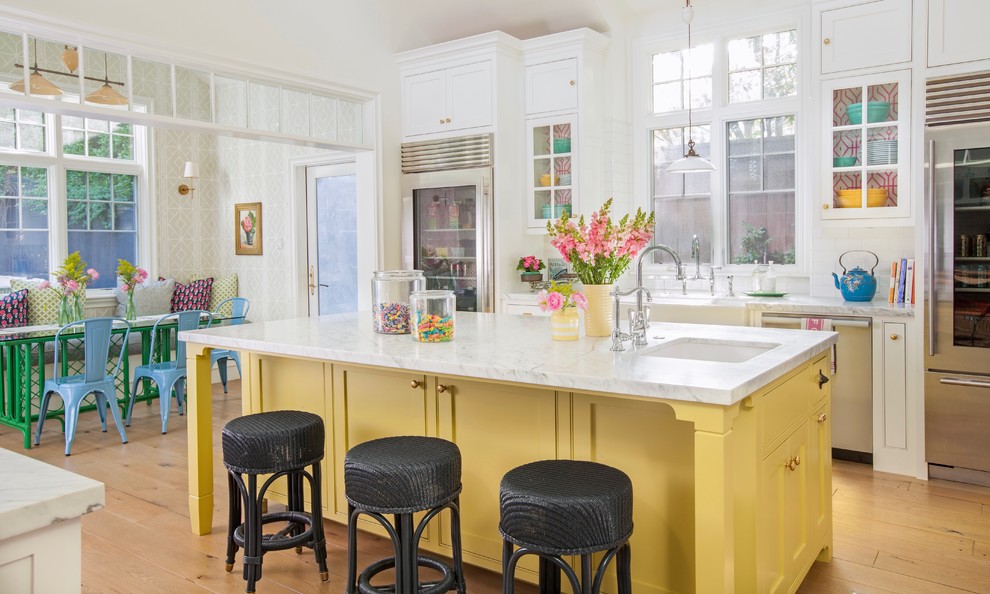 Expansive country galley kitchen in Los Angeles with a farmhouse sink, shaker cabinets, yellow cabinets, marble benchtops, white splashback, ceramic splashback, stainless steel appliances, light hardwood floors, with island and beige floor.