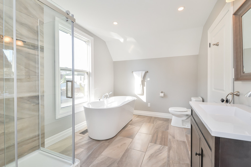 Large transitional master bathroom in Toronto with a freestanding tub, a corner shower, brown tile, ceramic tile, grey walls, ceramic floors, a drop-in sink, glass benchtops, shaker cabinets, dark wood cabinets and a one-piece toilet.