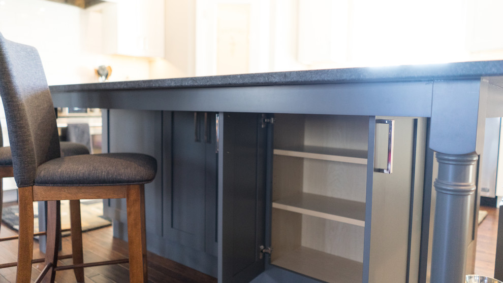 Example of a large transitional u-shaped eat-in kitchen design with a farmhouse sink, flat-panel cabinets, white cabinets, granite countertops, white backsplash, ceramic backsplash, stainless steel appliances and an island