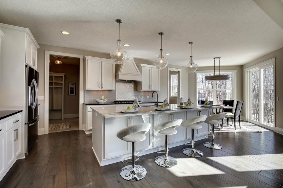 Example of a mid-sized transitional l-shaped dark wood floor open concept kitchen design in Minneapolis with a double-bowl sink, shaker cabinets, white cabinets, granite countertops, gray backsplash, subway tile backsplash, stainless steel appliances and an island