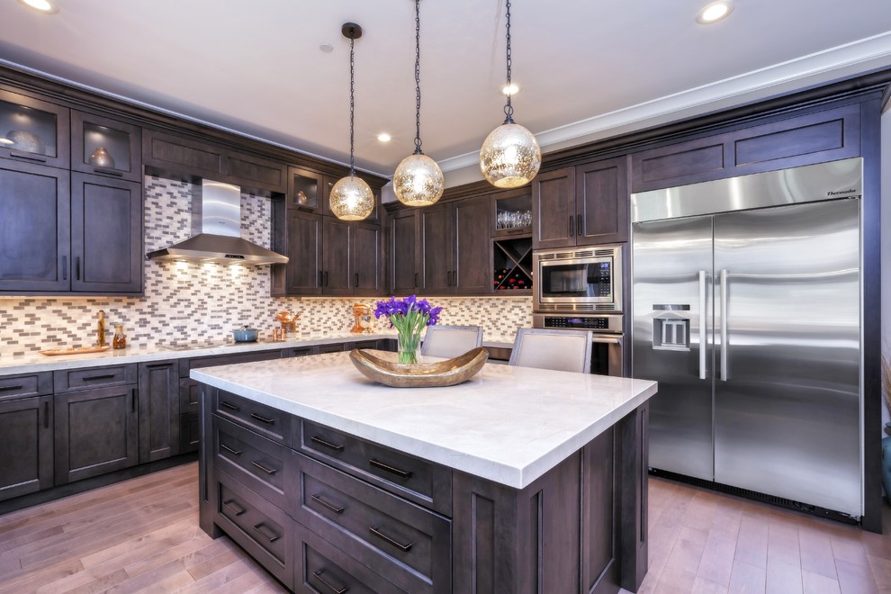 Large transitional u-shaped medium tone wood floor and brown floor eat-in kitchen photo with an undermount sink, recessed-panel cabinets, brown cabinets, marble countertops, multicolored backsplash, porcelain backsplash, stainless steel appliances and an island