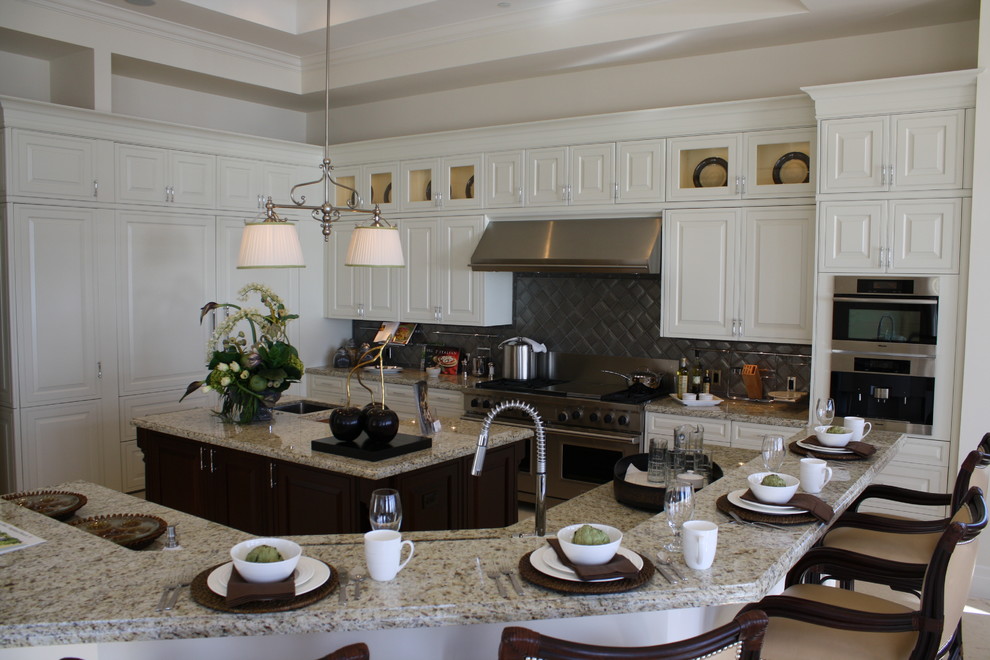 Inspiration for a large transitional u-shaped ceramic tile eat-in kitchen remodel in Miami with an undermount sink, raised-panel cabinets, white cabinets, granite countertops, gray backsplash, stone tile backsplash, stainless steel appliances and an island