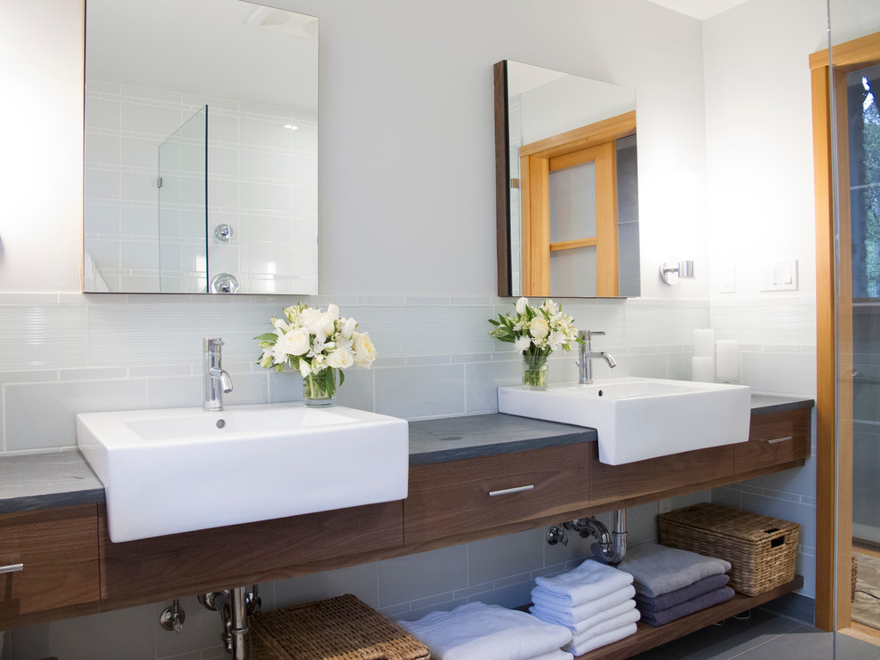 Photo of a small contemporary master bathroom in Seattle with flat-panel cabinets, dark wood cabinets, a curbless shower, gray tile, glass tile, white walls, porcelain floors, a two-piece toilet, an integrated sink and soapstone benchtops.
