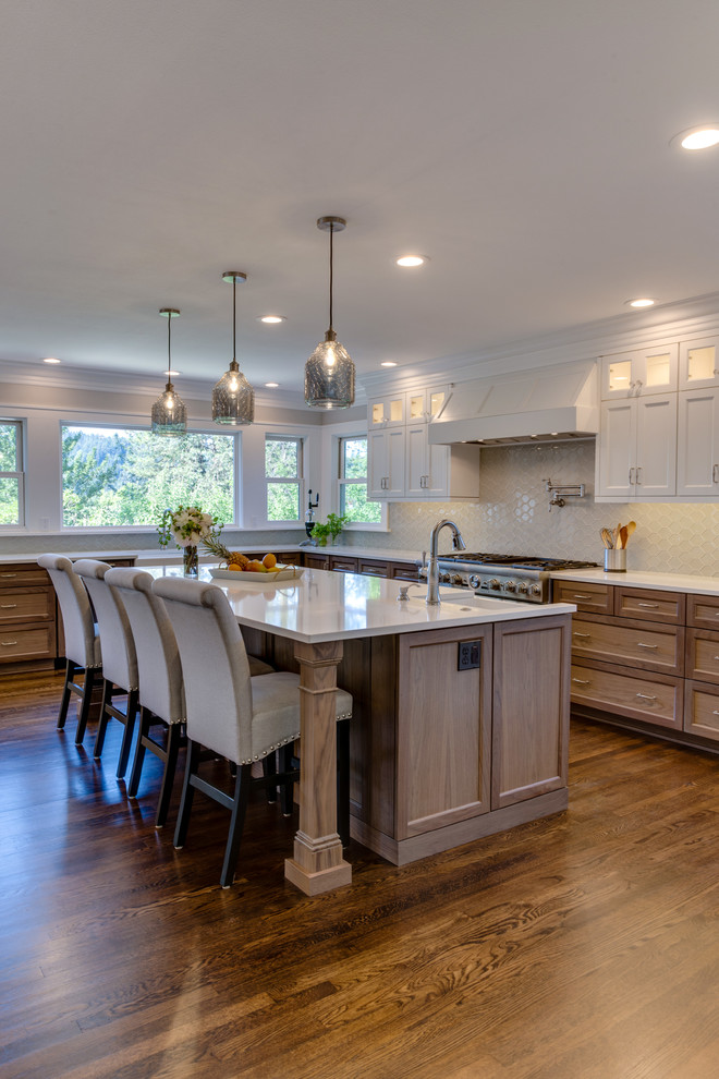Large country u-shaped open plan kitchen in Portland with a farmhouse sink, recessed-panel cabinets, medium wood cabinets, quartz benchtops, white splashback, glass tile splashback, stainless steel appliances, medium hardwood floors, with island, brown floor and white benchtop.
