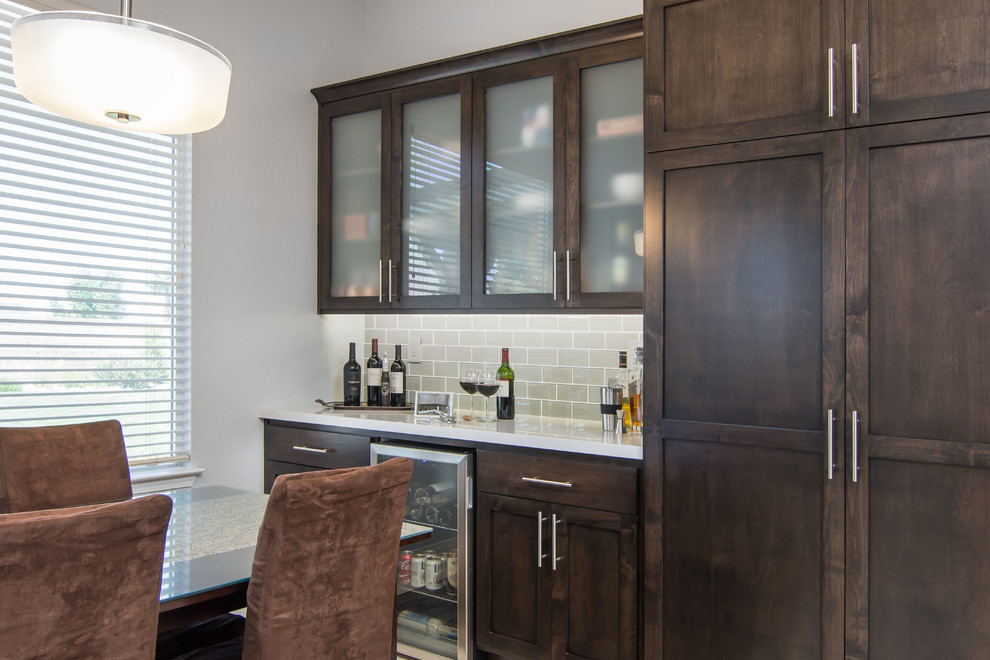 Photo of a mid-sized transitional single-wall home bar in Los Angeles with no sink, recessed-panel cabinets, dark wood cabinets, quartz benchtops, grey splashback, glass tile splashback, porcelain floors, beige floor and white benchtop.