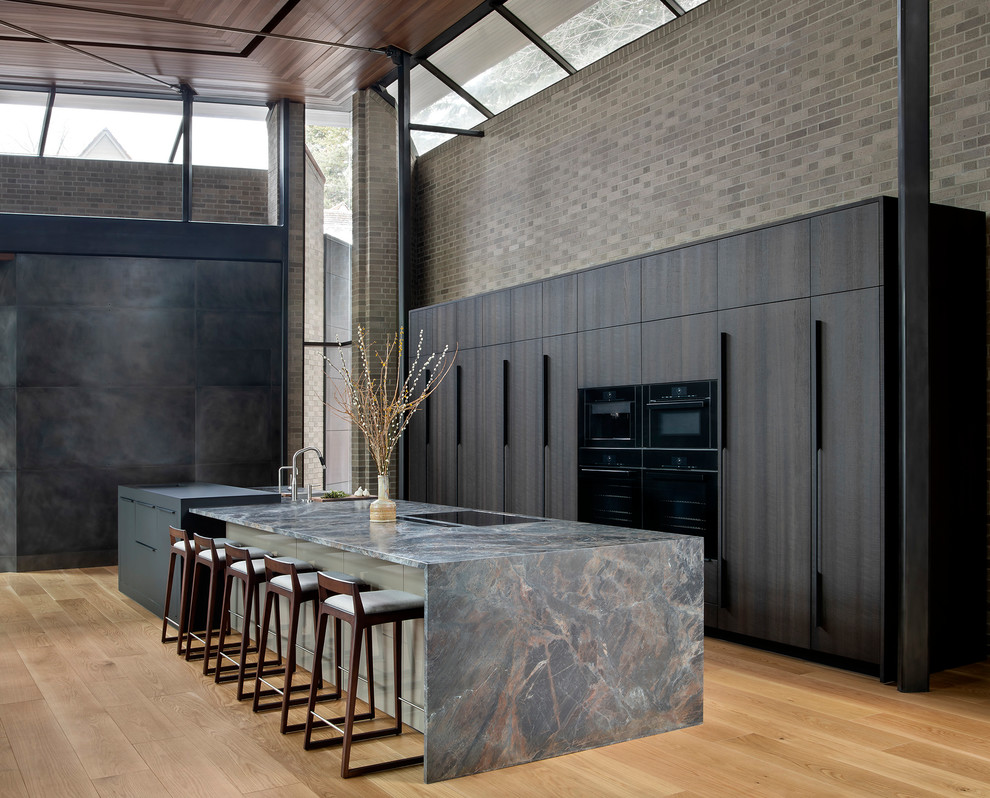 Contemporary l-shaped kitchen in Denver with flat-panel cabinets, dark wood cabinets, black appliances, medium hardwood floors, with island, brown floor and grey benchtop.