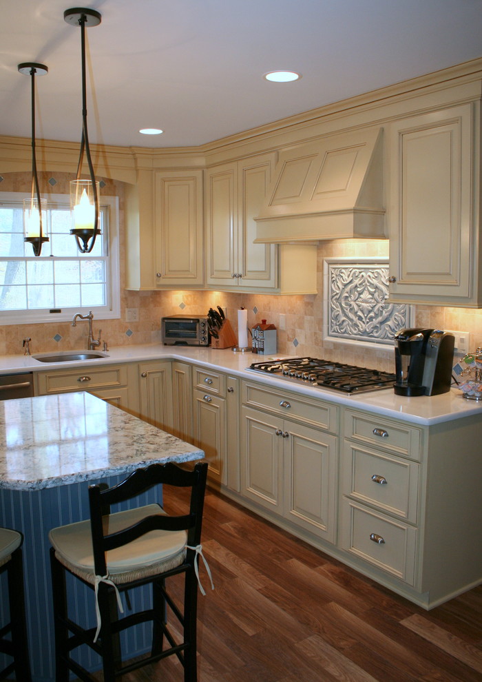 Photo of a mid-sized country l-shaped eat-in kitchen in New York with an undermount sink, raised-panel cabinets, yellow cabinets, quartzite benchtops, beige splashback, stainless steel appliances, porcelain floors and with island.