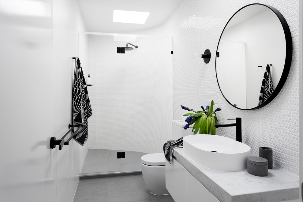Inspiration for a mid-sized contemporary 3/4 bathroom in Melbourne with flat-panel cabinets, white cabinets, an alcove shower, a one-piece toilet, white tile, mosaic tile, white walls, porcelain floors, a vessel sink, marble benchtops, grey floor and a hinged shower door.