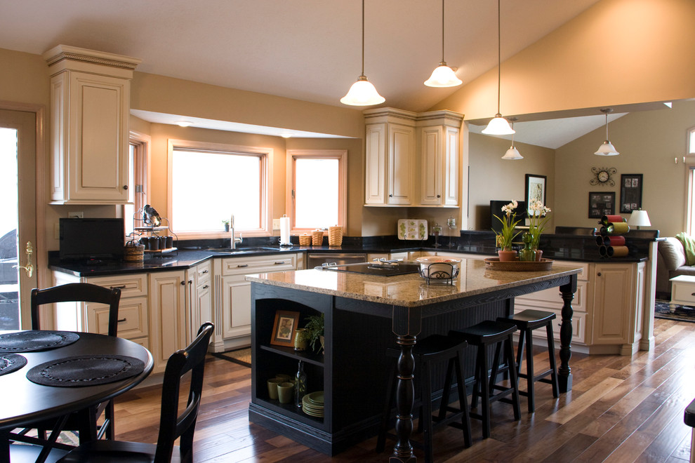 Large transitional l-shaped medium tone wood floor eat-in kitchen photo with an undermount sink, raised-panel cabinets, distressed cabinets, granite countertops, black backsplash, stainless steel appliances and an island