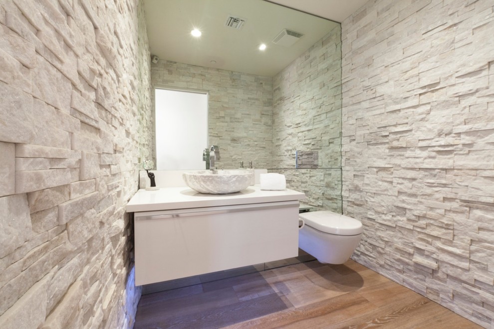 Inspiration for a mid-sized contemporary powder room in Phoenix with flat-panel cabinets, a wall-mount toilet, stone tile, light hardwood floors, a vessel sink, engineered quartz benchtops, white cabinets, white tile and white walls.