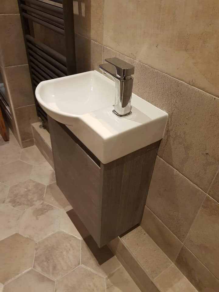 Inspiration for a small traditional powder room in Manchester with flat-panel cabinets, grey cabinets, a one-piece toilet, beige tile, ceramic tile, beige walls, ceramic floors, a wall-mount sink, beige floor and a floating vanity.