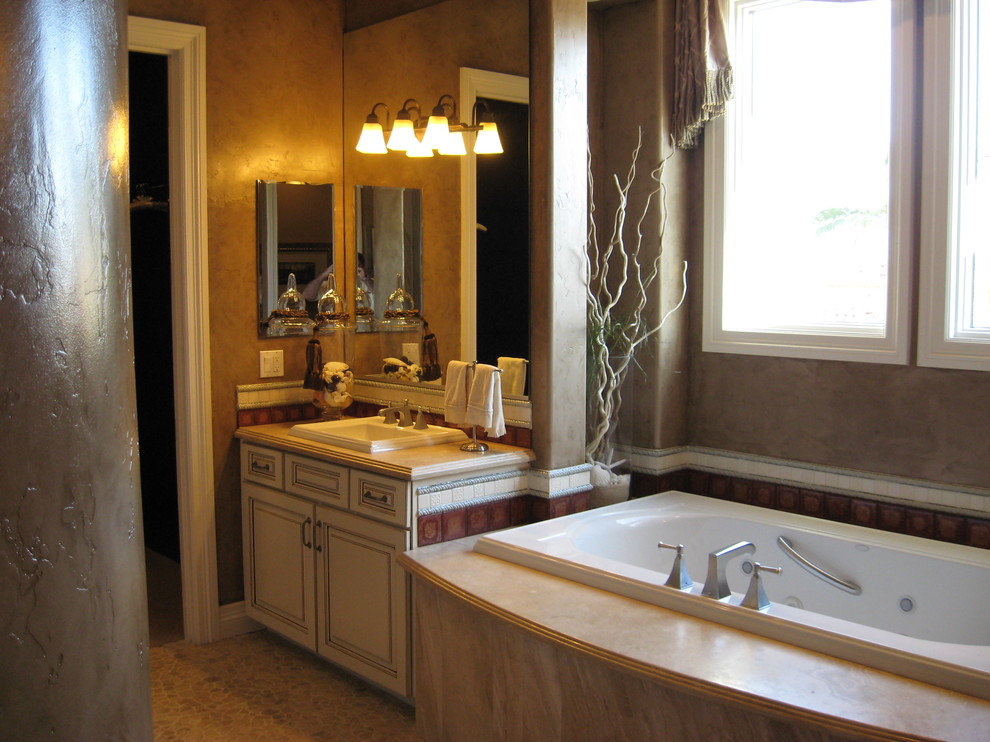 Large traditional master bathroom in Las Vegas with a drop-in sink, furniture-like cabinets, white cabinets, marble benchtops, a drop-in tub, a corner shower, a two-piece toilet, beige tile, stone tile, brown walls and pebble tile floors.
