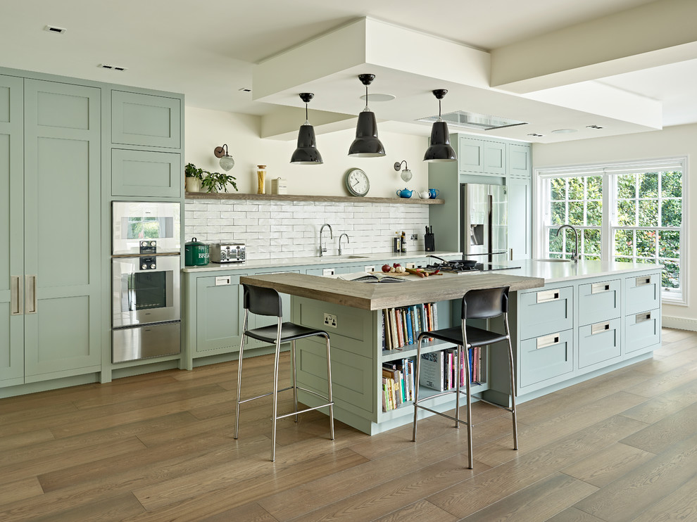 Photo of a large transitional single-wall open plan kitchen in London with a drop-in sink, shaker cabinets, green cabinets, quartzite benchtops, white splashback, subway tile splashback, stainless steel appliances, with island and white benchtop.