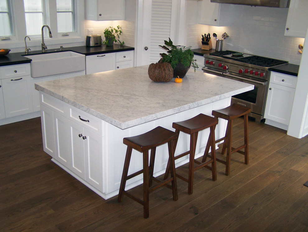 This is an example of a large transitional u-shaped eat-in kitchen in Los Angeles with a farmhouse sink, recessed-panel cabinets, white cabinets, white splashback, ceramic splashback, stainless steel appliances, dark hardwood floors and with island.