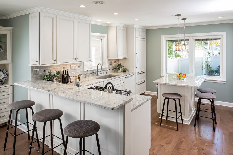 Inspiration for a mid-sized traditional u-shaped eat-in kitchen in Milwaukee with an undermount sink, recessed-panel cabinets, white cabinets, granite benchtops, beige splashback, subway tile splashback, stainless steel appliances, light hardwood floors and with island.