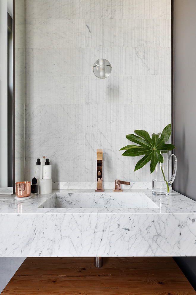 Inspiration for a mid-sized contemporary master wet room bathroom in London with furniture-like cabinets, medium wood cabinets, a drop-in tub, a one-piece toilet, gray tile, marble, grey walls, porcelain floors, a wall-mount sink, marble benchtops, grey floor and an open shower.