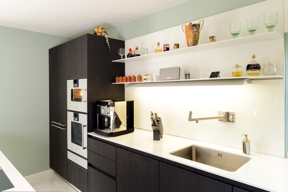 Design ideas for a mid-sized contemporary single-wall kitchen in Hanover with an undermount sink, flat-panel cabinets, dark wood cabinets, white splashback, glass sheet splashback and panelled appliances.