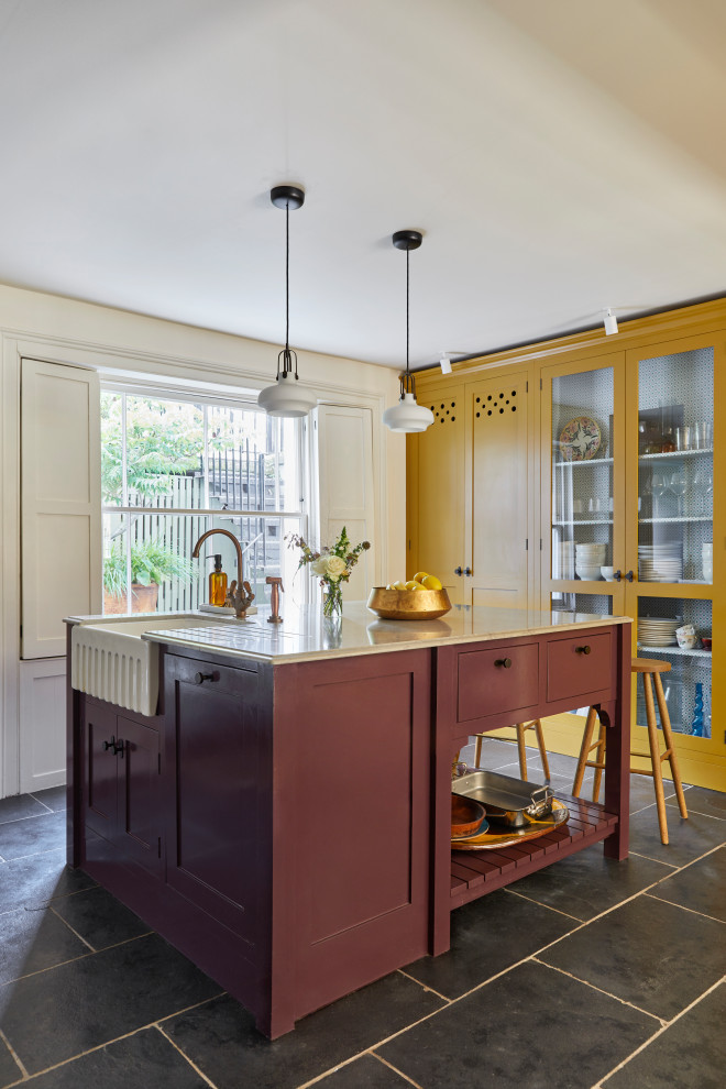 Inspiration for a large transitional eat-in kitchen in London with a farmhouse sink, shaker cabinets, yellow cabinets, marble benchtops, white splashback, ceramic splashback, white appliances, limestone floors, with island, black floor and brown benchtop.