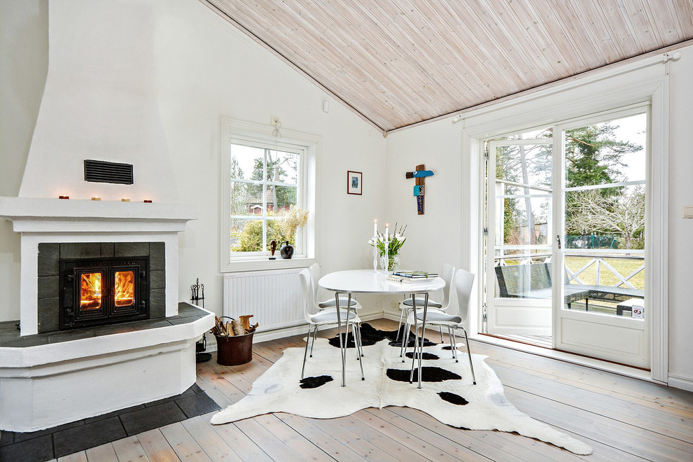This is an example of a large scandinavian dining room in Stockholm with white walls, light hardwood floors and a wood stove.