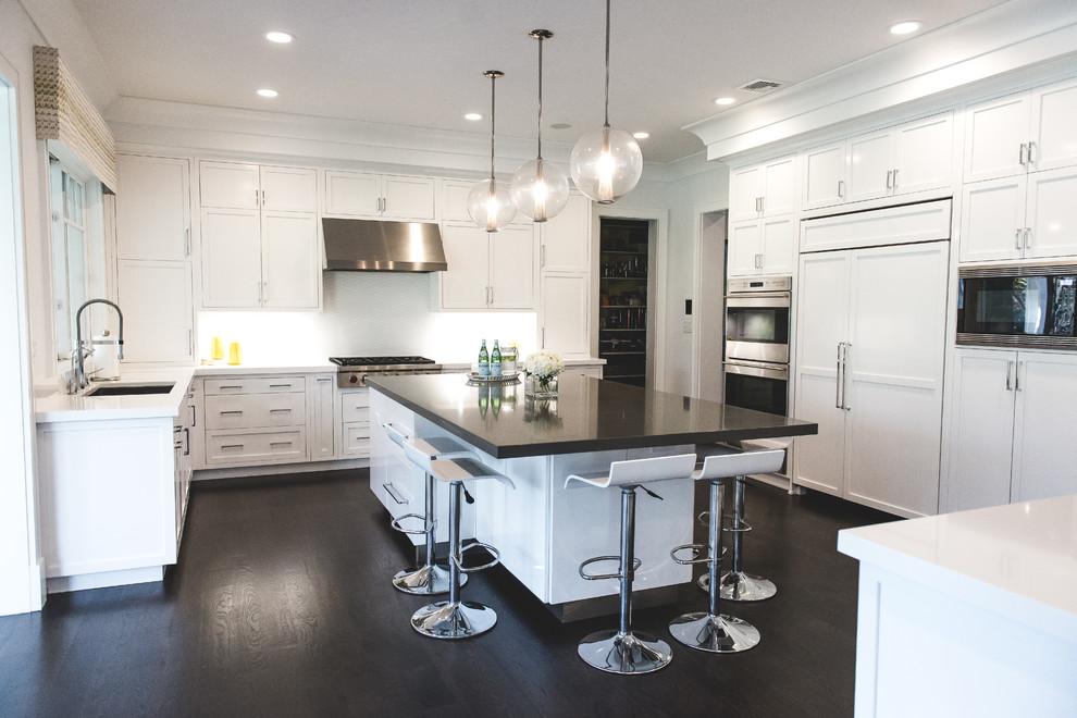 Photo of a large transitional u-shaped eat-in kitchen in New York with an undermount sink, shaker cabinets, white cabinets, white splashback, stainless steel appliances, dark hardwood floors, with island, solid surface benchtops and ceramic splashback.