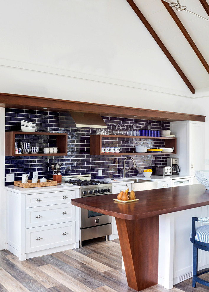This is an example of a beach style kitchen in Boston with a farmhouse sink, open cabinets, dark wood cabinets, wood benchtops, blue splashback, subway tile splashback, stainless steel appliances and with island.