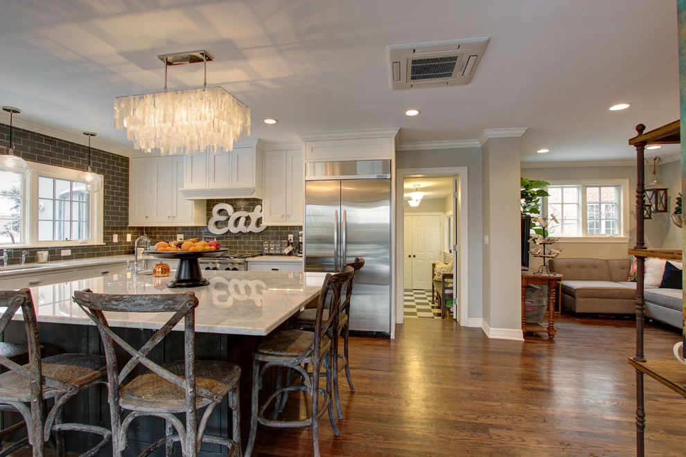 Example of a large transitional l-shaped dark wood floor enclosed kitchen design in Denver with an undermount sink, shaker cabinets, white cabinets, marble countertops, brown backsplash, subway tile backsplash, stainless steel appliances and an island