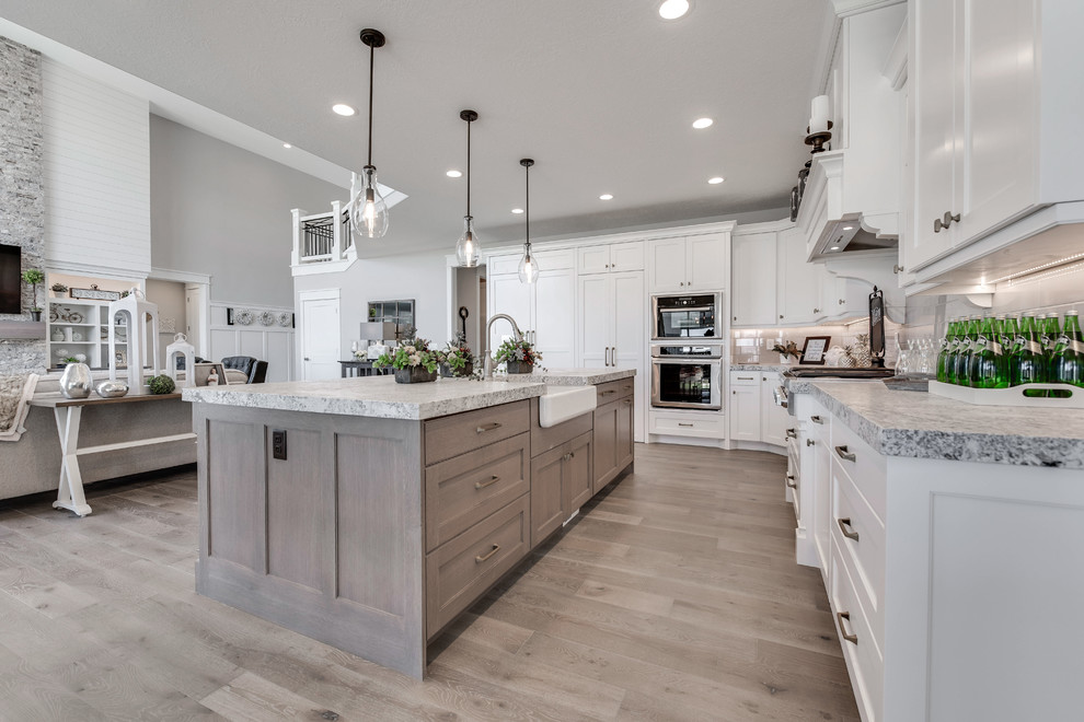 Photo of a mid-sized arts and crafts l-shaped open plan kitchen in Salt Lake City with a farmhouse sink, shaker cabinets, white cabinets, marble benchtops, white splashback, subway tile splashback, panelled appliances, medium hardwood floors, with island and brown floor.