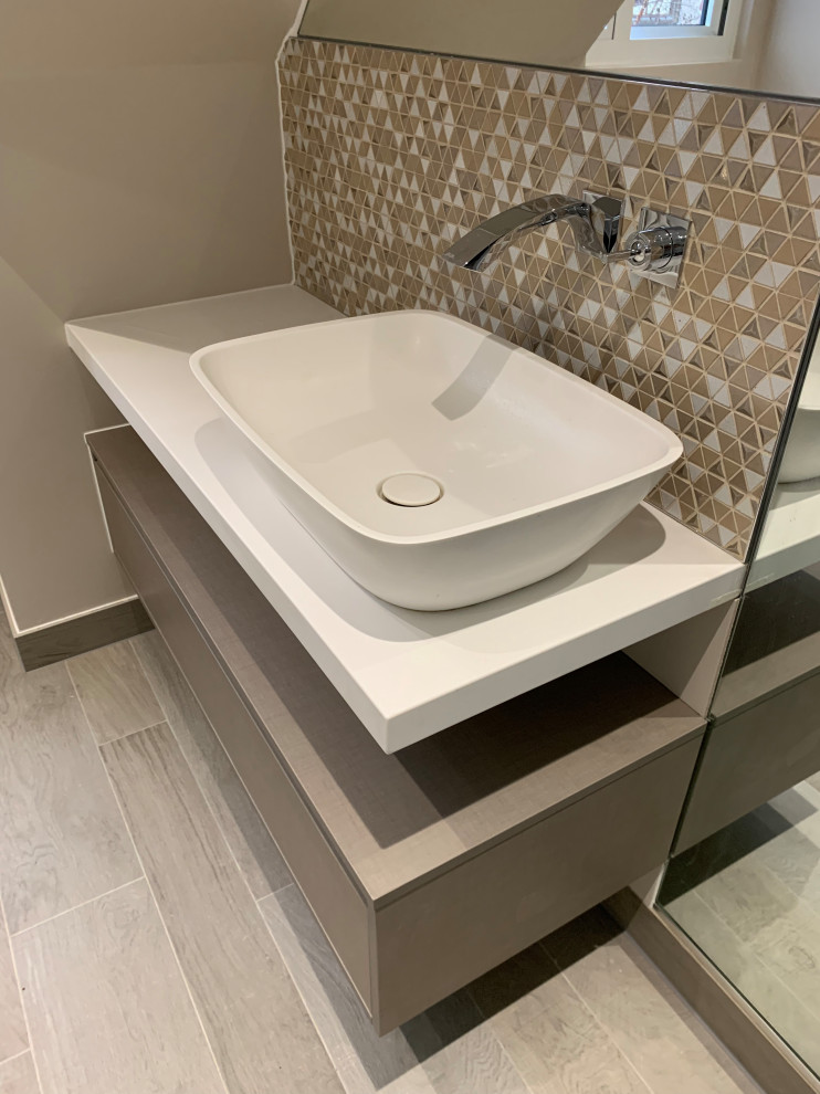 This is an example of a mid-sized scandinavian kids wet room bathroom in London with flat-panel cabinets, beige cabinets, a wall-mount toilet, beige tile, porcelain tile, beige walls, porcelain floors, a console sink, solid surface benchtops, brown floor, a hinged shower door, white benchtops, a niche, a single vanity and a floating vanity.