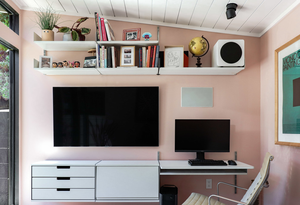 Photo of a small midcentury home studio in Los Angeles with pink walls, vinyl floors, a built-in desk and brown floor.