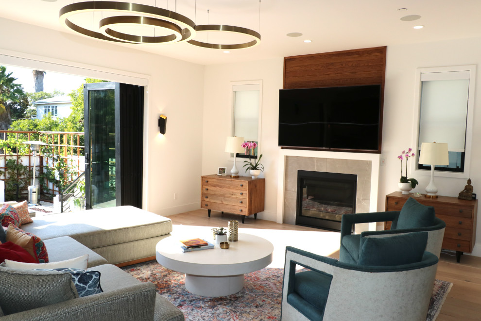 На фото: большая гостиная комната в современном стиле с с книжными шкафами и полками, белыми стенами, светлым паркетным полом, стандартным камином, телевизором на стене и коричневым полом с