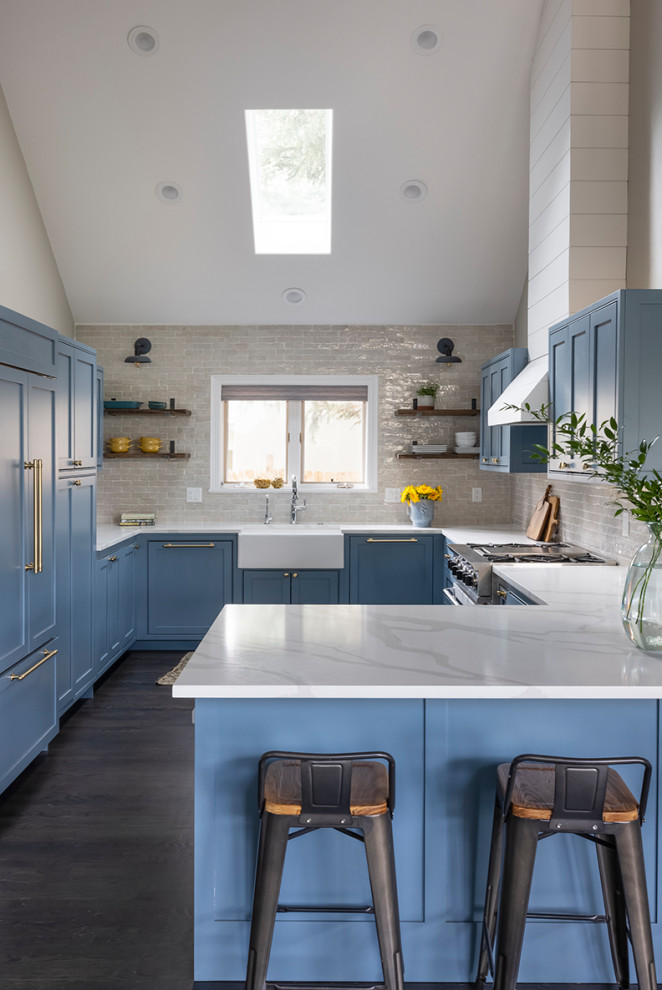 This is an example of a medium sized rural u-shaped kitchen in Denver with a belfast sink, shaker cabinets, blue cabinets, engineered stone countertops, white splashback, metro tiled splashback, integrated appliances, dark hardwood flooring, brown floors, white worktops and a vaulted ceiling.