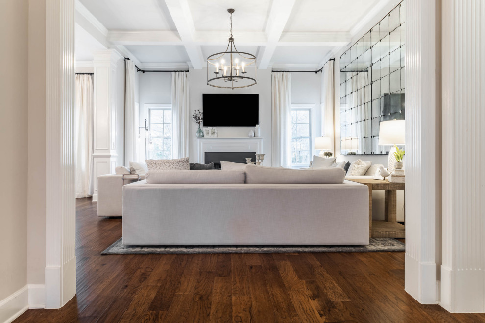 Mid-sized transitional open concept living room in Nashville with white walls, medium hardwood floors, a standard fireplace, a wall-mounted tv, brown floor and coffered.