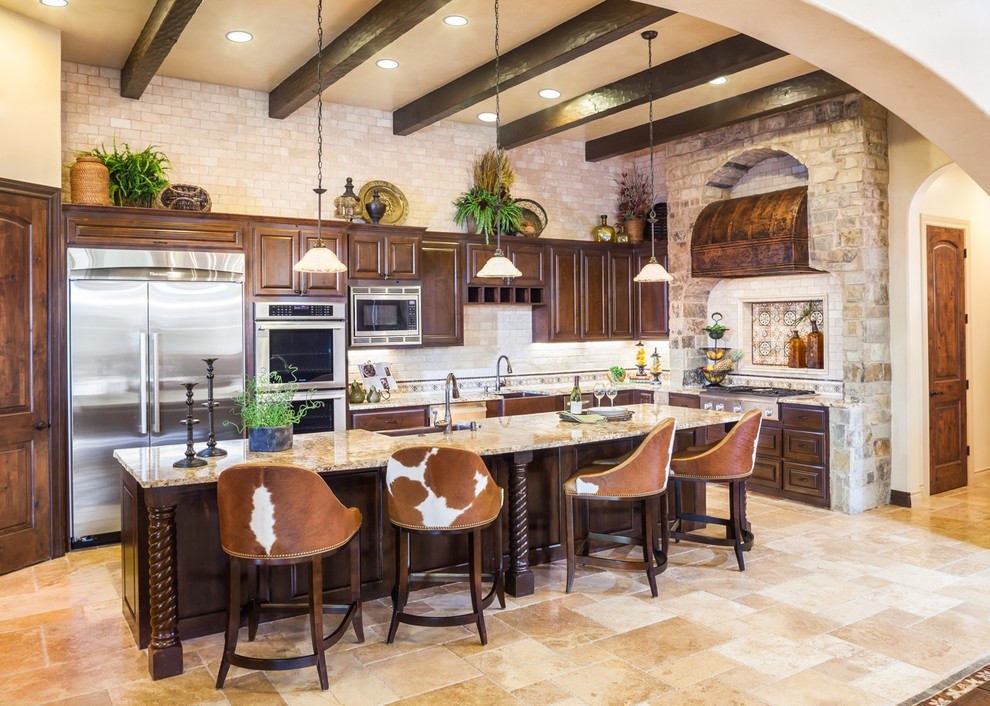 This is an example of a large mediterranean l-shaped open plan kitchen in Houston with a farmhouse sink, raised-panel cabinets, dark wood cabinets, beige splashback, stainless steel appliances, with island, beige floor, granite benchtops, travertine floors and beige benchtop.