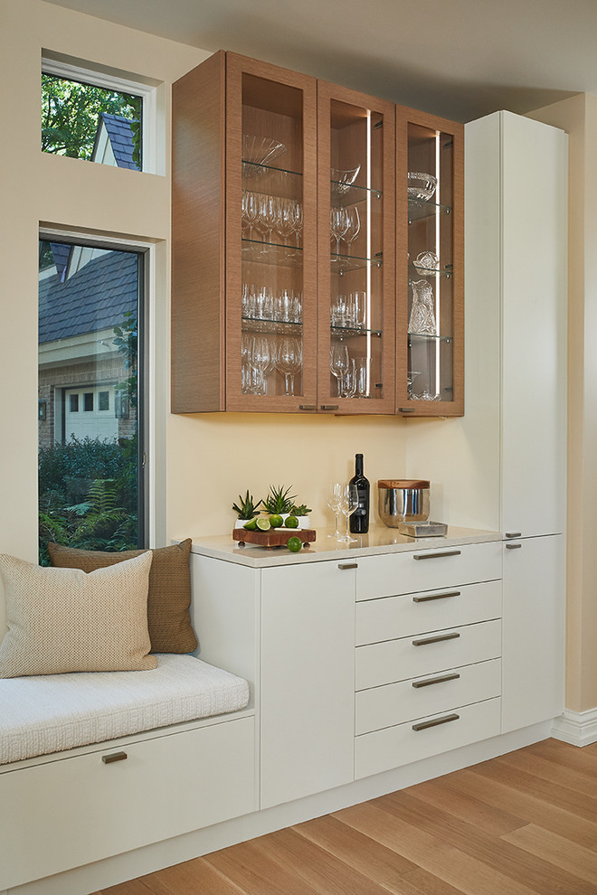 Transitional single-wall light wood floor and beige floor dry bar photo with no sink, glass-front cabinets, light wood cabinets, beige backsplash and beige countertops