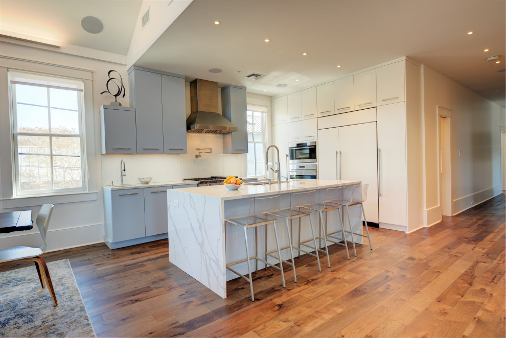 Inspiration for a mid-sized contemporary l-shaped kitchen in New Orleans with an undermount sink, flat-panel cabinets, blue cabinets, white splashback, panelled appliances, medium hardwood floors, with island and white benchtop.