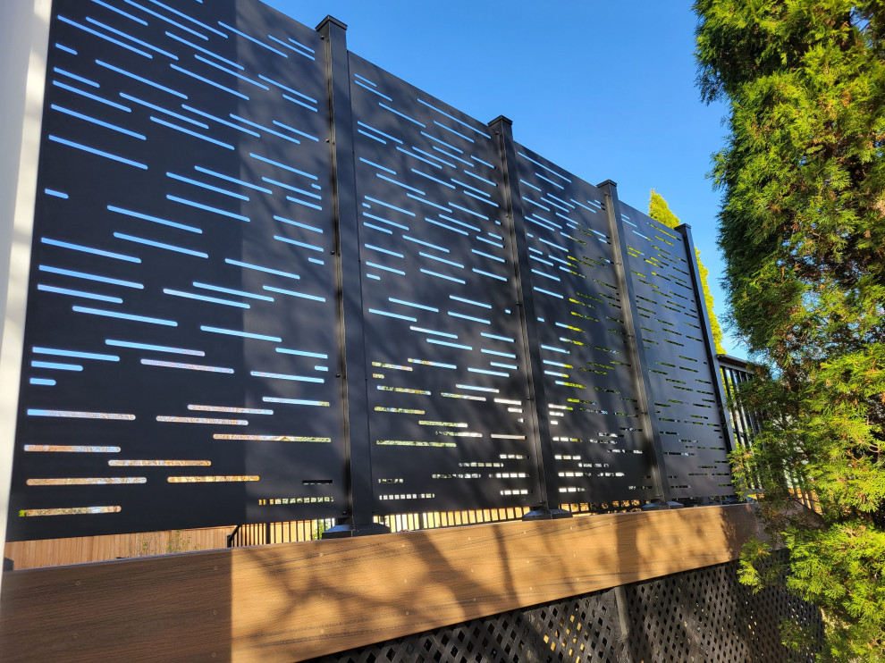 Example of a mid-sized backyard ground level privacy and metal railing deck design with no cover
