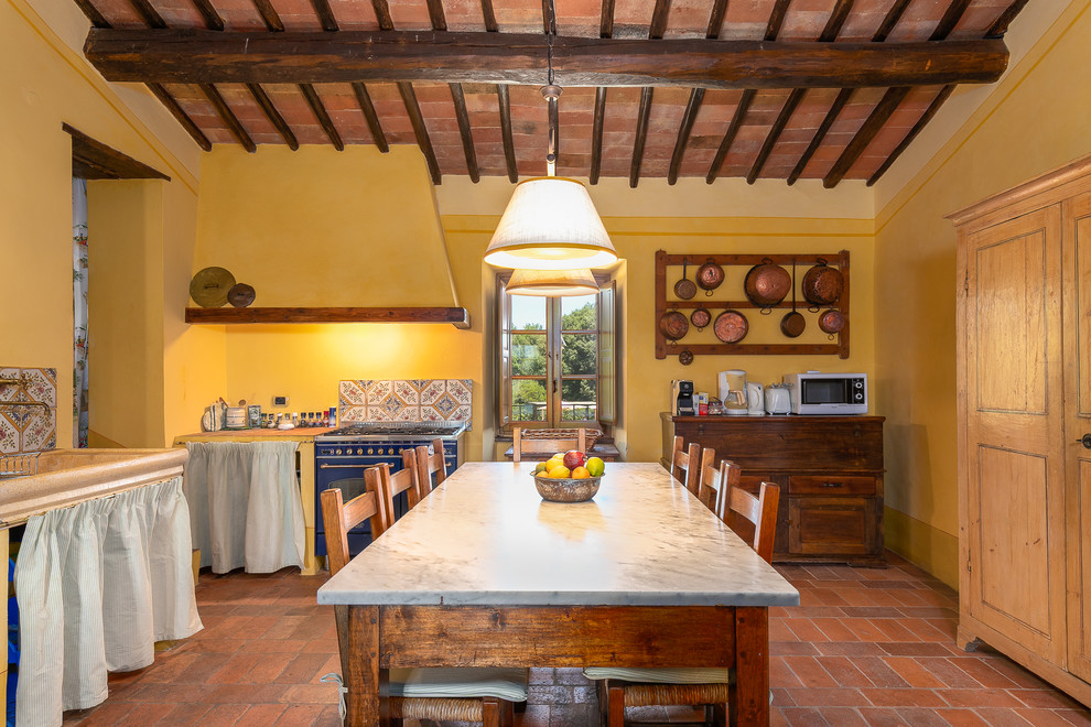 Mediterranean separate kitchen in Florence with coloured appliances, terra-cotta floors, with island, orange floor and grey benchtop.