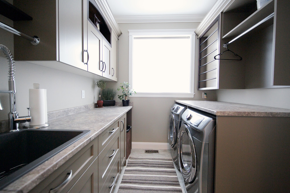 Design ideas for a mid-sized traditional galley dedicated laundry room in Vancouver with a drop-in sink, shaker cabinets, laminate benchtops, grey walls, porcelain floors, a side-by-side washer and dryer and grey cabinets.