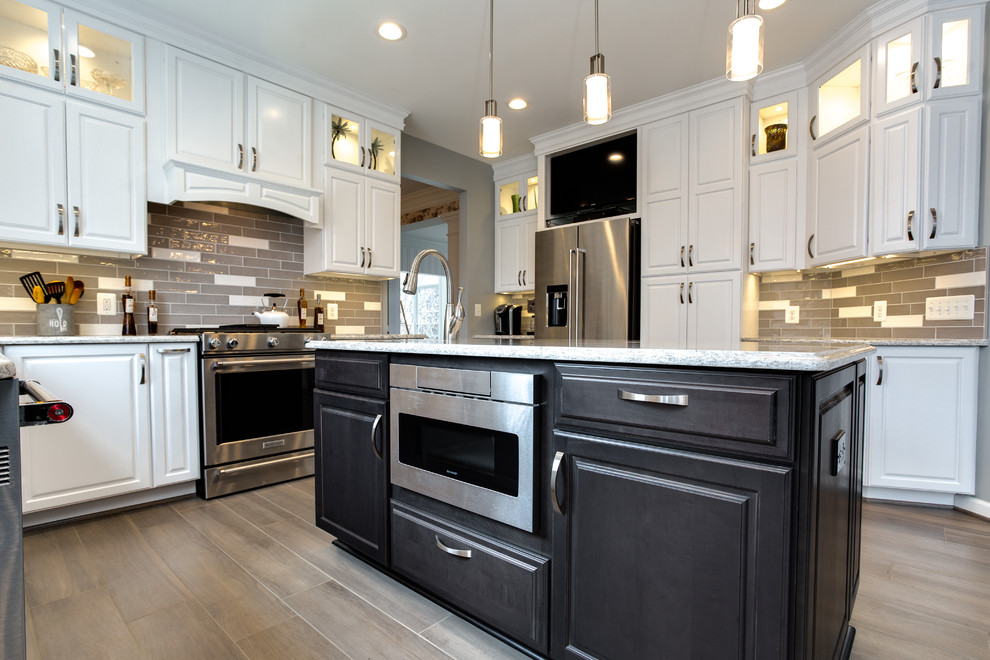 Eat-in kitchen - large transitional u-shaped porcelain tile and brown floor eat-in kitchen idea in DC Metro with a single-bowl sink, raised-panel cabinets, white cabinets, quartz countertops, gray backsplash, ceramic backsplash, stainless steel appliances and an island