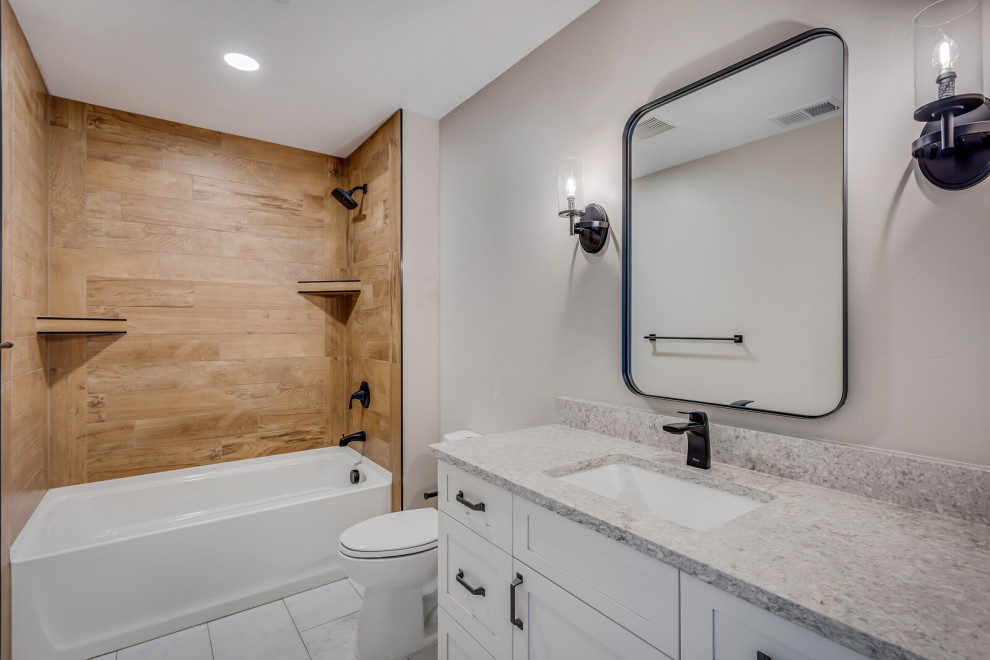 This is an example of a mid-sized country kids bathroom in Other with recessed-panel cabinets, white cabinets, an alcove tub, a shower/bathtub combo, a two-piece toilet, brown tile, wood-look tile, grey walls, ceramic floors, an undermount sink, engineered quartz benchtops, white floor, a shower curtain, grey benchtops, a single vanity and a built-in vanity.