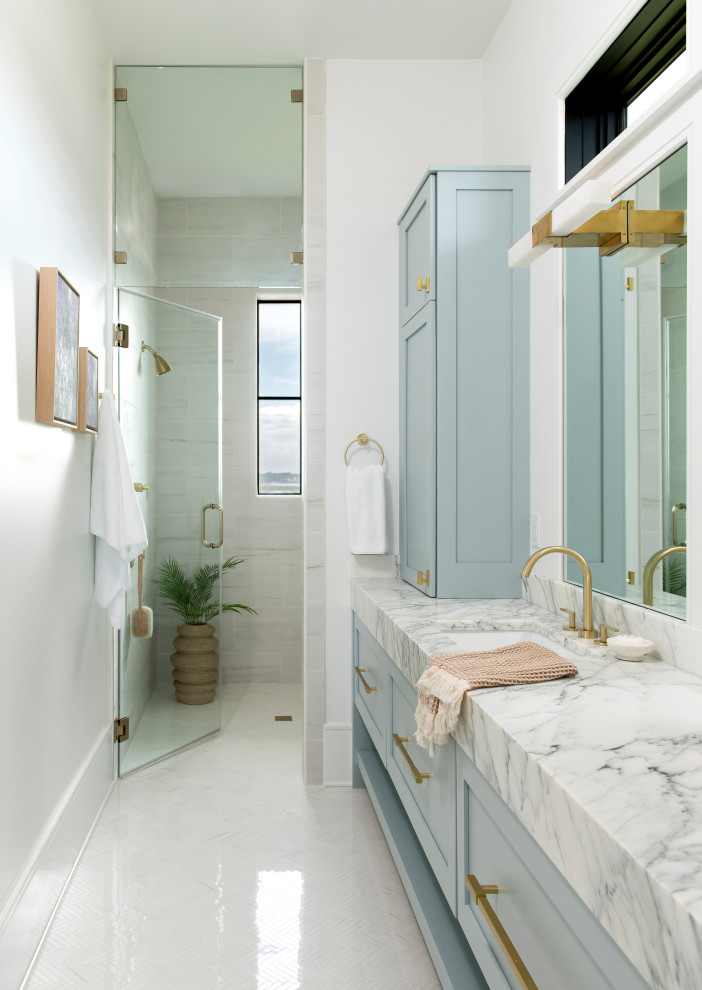Beach style gray tile white floor walk-in shower photo with shaker cabinets, blue cabinets, white walls, an undermount sink, a hinged shower door, white countertops and a built-in vanity