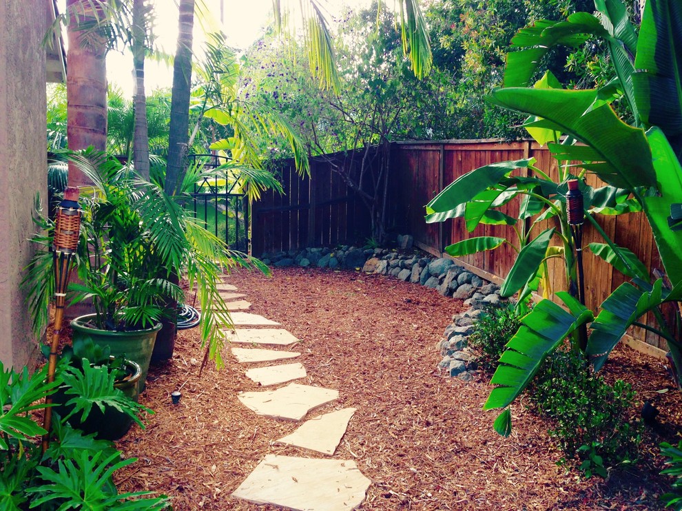 This is an example of a small tropical side yard partial sun garden in San Diego with a garden path and natural stone pavers.