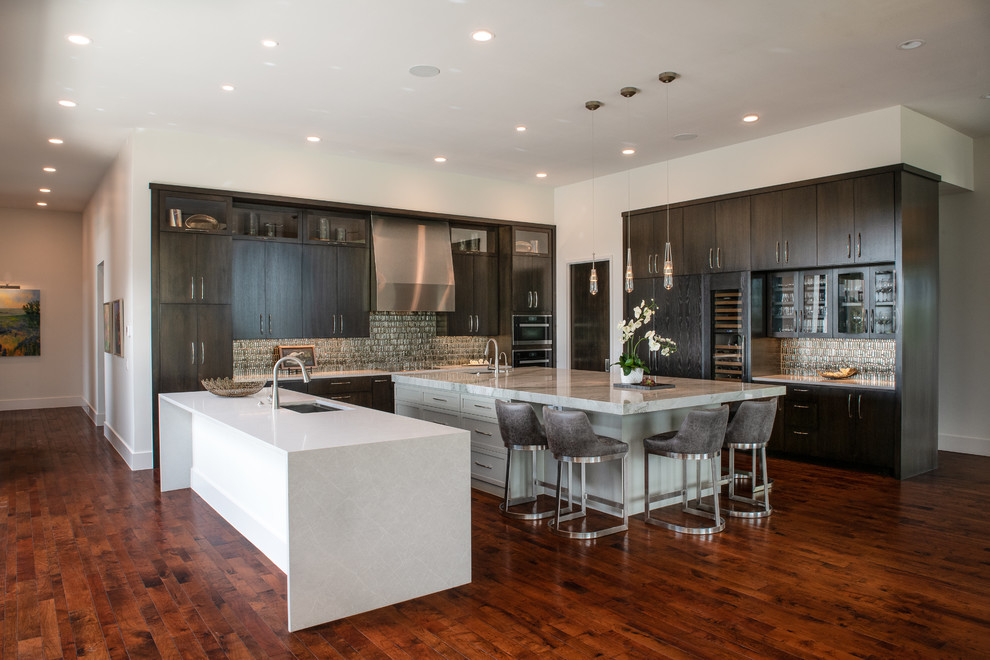 Contemporary l-shaped open plan kitchen in Austin with flat-panel cabinets, brown cabinets, multiple islands, white benchtop, an undermount sink, green splashback, mosaic tile splashback, stainless steel appliances, dark hardwood floors and brown floor.